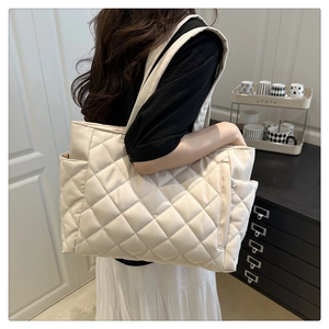 Detail of a large cream quilted tote bag showing side pockets and diamond stitch pattern