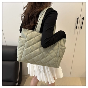 Close-up of light green quilted tote bag with diamond pattern and side pocket on a model