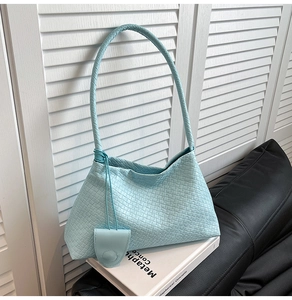 Gros plan d'un sac hobo tressé bleu clair avec mini charme à rabat sur fond de volet blanc