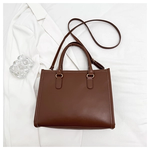 Detailed view of brown leather tote bag with gold metal rings and adjustable shoulder strap