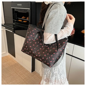 Vue latérale d'un sac cabas noir à motif cerises porté à l'épaule dans un décor de vie quotidien