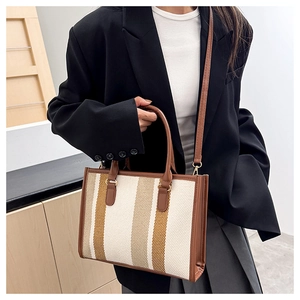 Close-up of a striped canvas tote bag with brown leather handles and gold-tone hardware