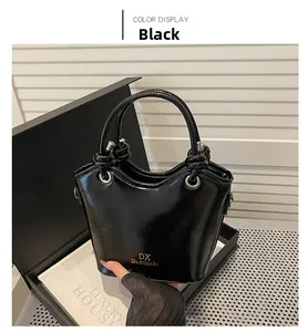 Detail einer schwarzen glänzenden Beuteltasche mit Goldlogo und Knotengriff in Box