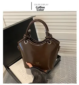 Details der kaffeebraunen Lackleder-Handtasche mit Knotengriff und goldenem Logo-Akzent