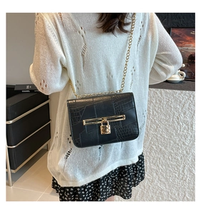 Detail of black textured leather bag featuring gold heart padlock and chain strap