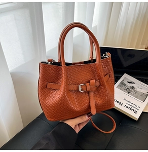 Détail du sac à main marron tissé avec boucle argentée posé sur un tabouret en cuir
