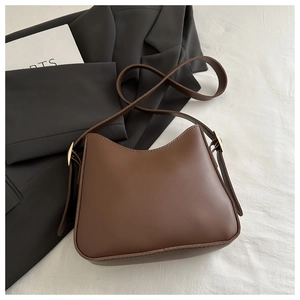 Flat lay of brown matte leather shoulder bag with gold buckles on white fabric