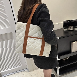 Large white quilted puffer tote bag with brown straps shown on shoulder in a modern setting