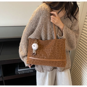 Detail of leopard print tote bag with brown leather straps and white plush doll charm