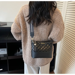 Close-up of quilted black crossbody bag with gold FASHION logo and patterned wide strap