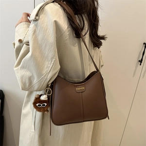 Brown matte leather shoulder bag with trapezoidal design and plush monster charm decoration