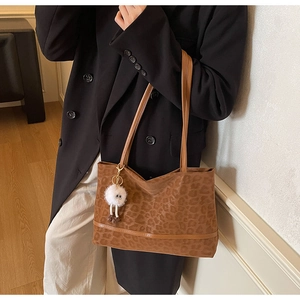 Close-up of a large leopard print tote bag featuring a leather strap and plush charm