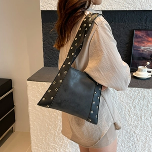 Sac à bandoulière noir avec rivets dorés porté par un mannequin dans un café chic