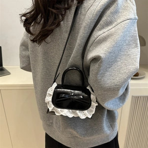 Chic black mini crossbody bag with white lace trim and bow accent worn by model