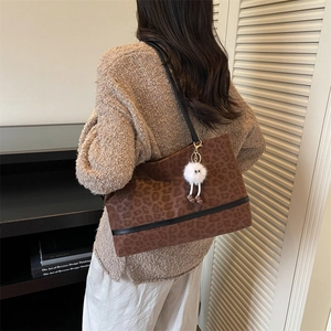 Large leopard print tote bag with plush monster charm and black straps on a female model