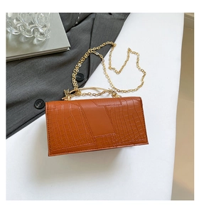 Detailed macro view of orange crocodile-patterned bag with gold chain and metal handle