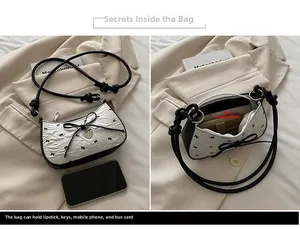 Dettaglio della borsa a mezzaluna bianca plissettata con fiocchi neri e ciondolo a cuore