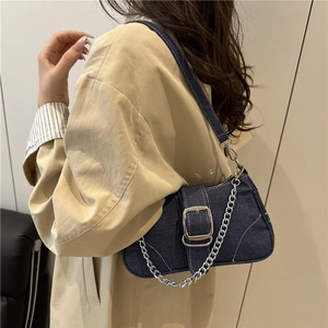 Sac baguette chic en denim bleu foncé avec boucle argentée et chaîne porté à l'épaule