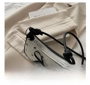 Dettaglio della cerniera in metallo e fiocco nero sulla borsa bianca in seersucker