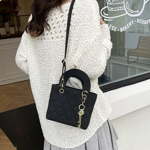 Elegant black quilted handbag with gold key charm and adjustable strap shown on model