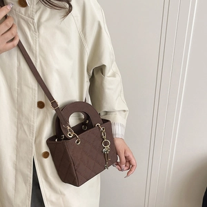 Deep brown quilted handbag with gold hardware and charm shown on a model's shoulder