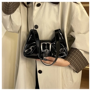 Close-up of black patent leather shoulder bag with large silver buckles and glossy finish
