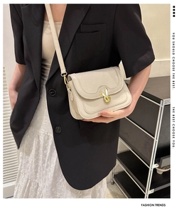 Detail of a beige leather crossbody bag featuring a golden rabbit-shaped metal turn-lock