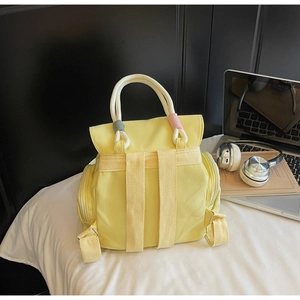 Detail of yellow fabric backpack featuring white rope handles and colorful embroidery accents