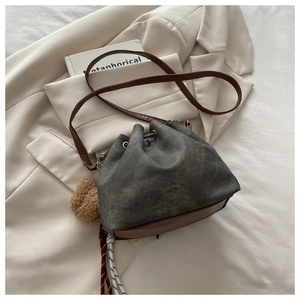 Detail of gray canvas bucket bag with brown leather base and cute plush bear charm