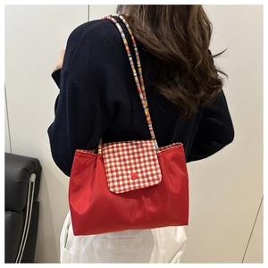 Détail du sac rouge avec rabat à carreaux rouges et blancs et bandoulière tissée