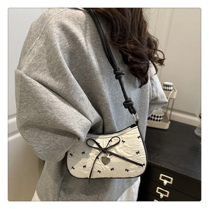 Détail du sac blanc à nœud avec texture gaufrée, pendentif cœur et bandoulière nouée