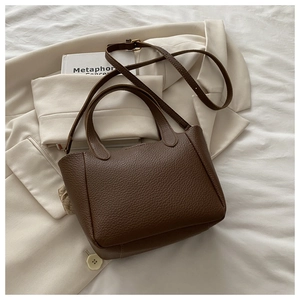 Close-up of brown litchi grain leather texture and handle on a minimalist bucket bag