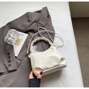 Detail of a creamy white pleated handbag with lace decoration and a detachable strap