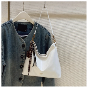Close-up of white patent leather hobo bag with fashion text and braided rope charm