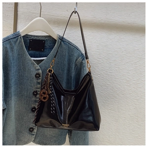 Detail of black patent leather underarm bag with gold logo and stylish scarf charm