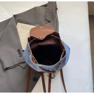 Detail of denim and brown leather backpack with silver chain drawstring and fabric lining