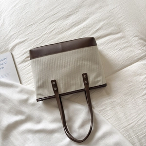 Detail of beige woven tote bag with dark brown leather handles and silver studs