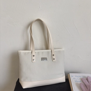 Detail of woven texture and silver metal brand logo on beige tote shoulder bag