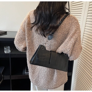 Close-up of black crocodile-embossed baguette bag with woven shoulder strap and metal clasp