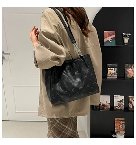 Detail of black leather tote bag with bear pattern worn by model in casual setting