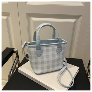 Close-up of light blue checkered tote bag with matching leather straps on white pedestal