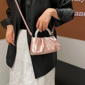 Pink pleated cloud bag with pearl handle and shoulder strap worn by a model in a trendy outfit