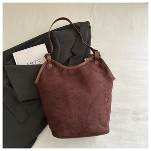 Detail of a large dark brown suede tote bag with leather trim on white fabric background