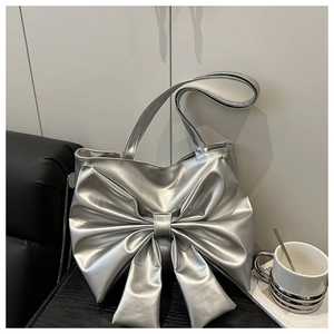 Close-up of a silver bow shoulder bag with glossy metallic finish on a modern black sofa