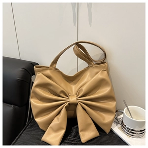 Detail of khaki bow-shaped handbag with premium faux leather texture on wooden table