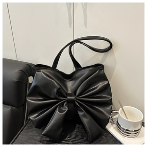 Detail of a black tote bag featuring a large decorative bow and soft pleated texture