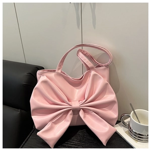 Detail of pink faux leather tote bag featuring a large bow design on black wooden table