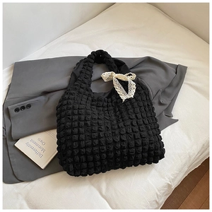 Detail shot of black puffy bubble texture tote bag with white lace ribbon bow on white bedding