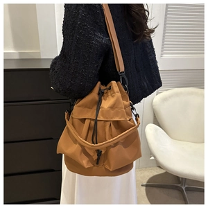 Brown drawstring bucket bag shown worn crossbody style by a model in a casual setting