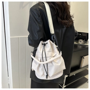 Detail view of cream drawstring bucket bag with pleated design and wide shoulder strap